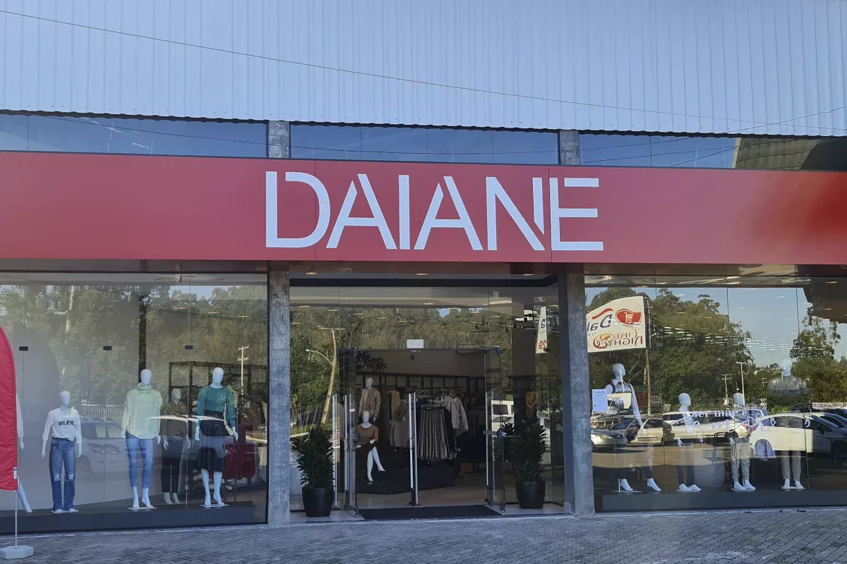 Obras casa Daiane Portão - Fachada de loja com letreiro Daiane, grandes portas de vidro, área ajardinada e ambientes planejados, destacando atendimento consultivo e Soluções em Comunicação inovadoras.