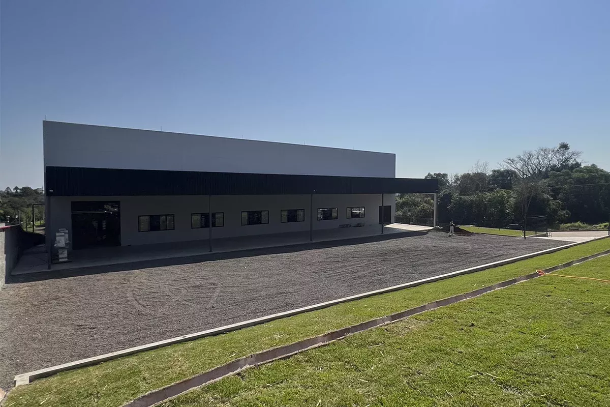 Obras casa Dass - Perspectiva externa do galpão industrial, pátio pavimentado, gramado lateral e estrutura robusta, ressaltando eficiência logística e alinhamento estratégico com objetivos de negócio.