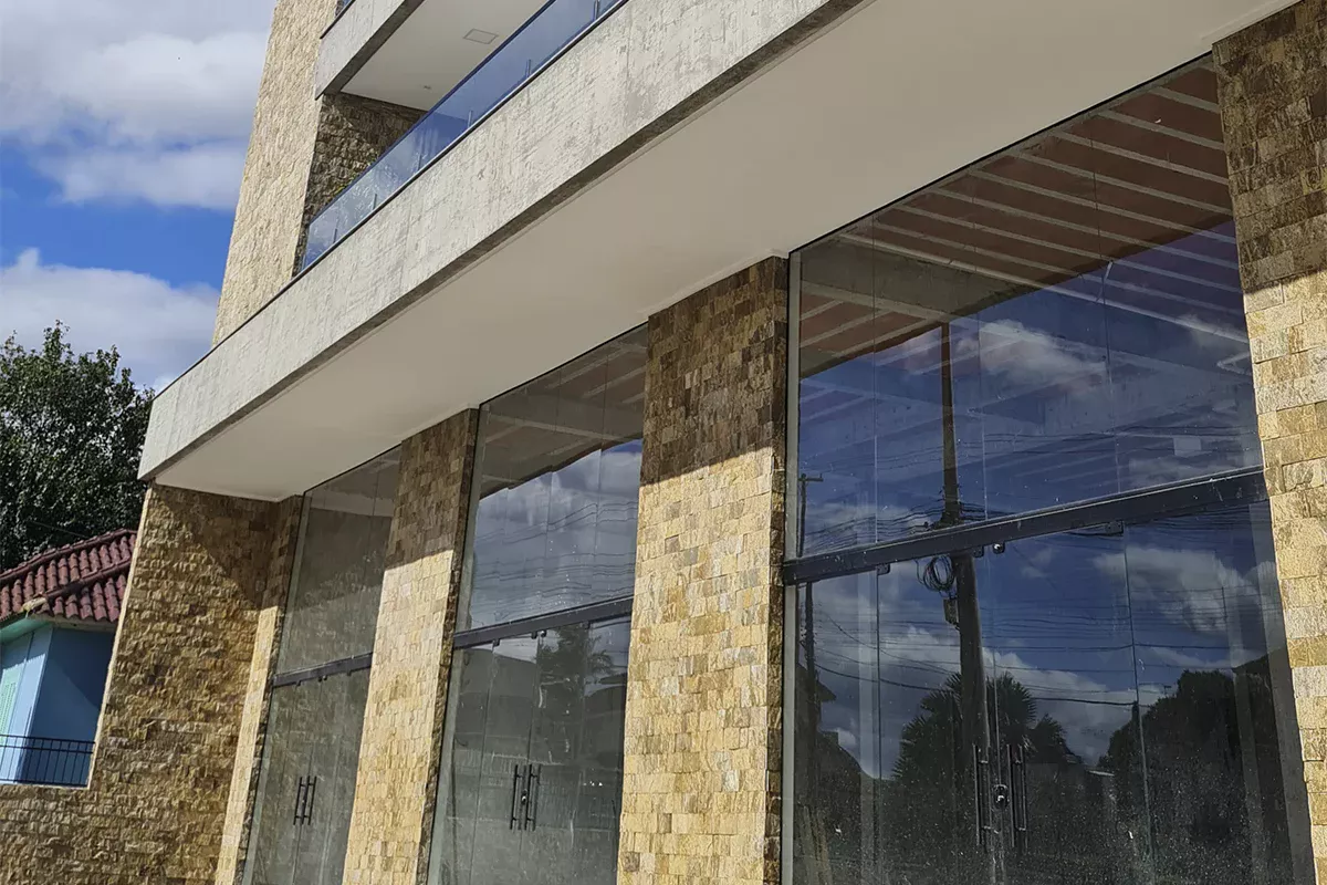 Obras casa Friedbert - Detalhe de fachada comercial com pilares revestidos em pedra e amplas áreas envidraçadas, destacando padrão elevado e Soluções em Comunicação alinhadas ao cliente.