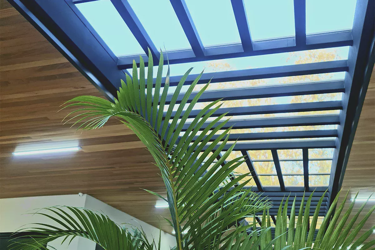 Obras casa Green Garden - Detalhe do pergolado em estrutura metálica azul, paisagismo integrado e madeira aparente, transmitindo inovação arquitetônica e foco em ambientes funcionais.