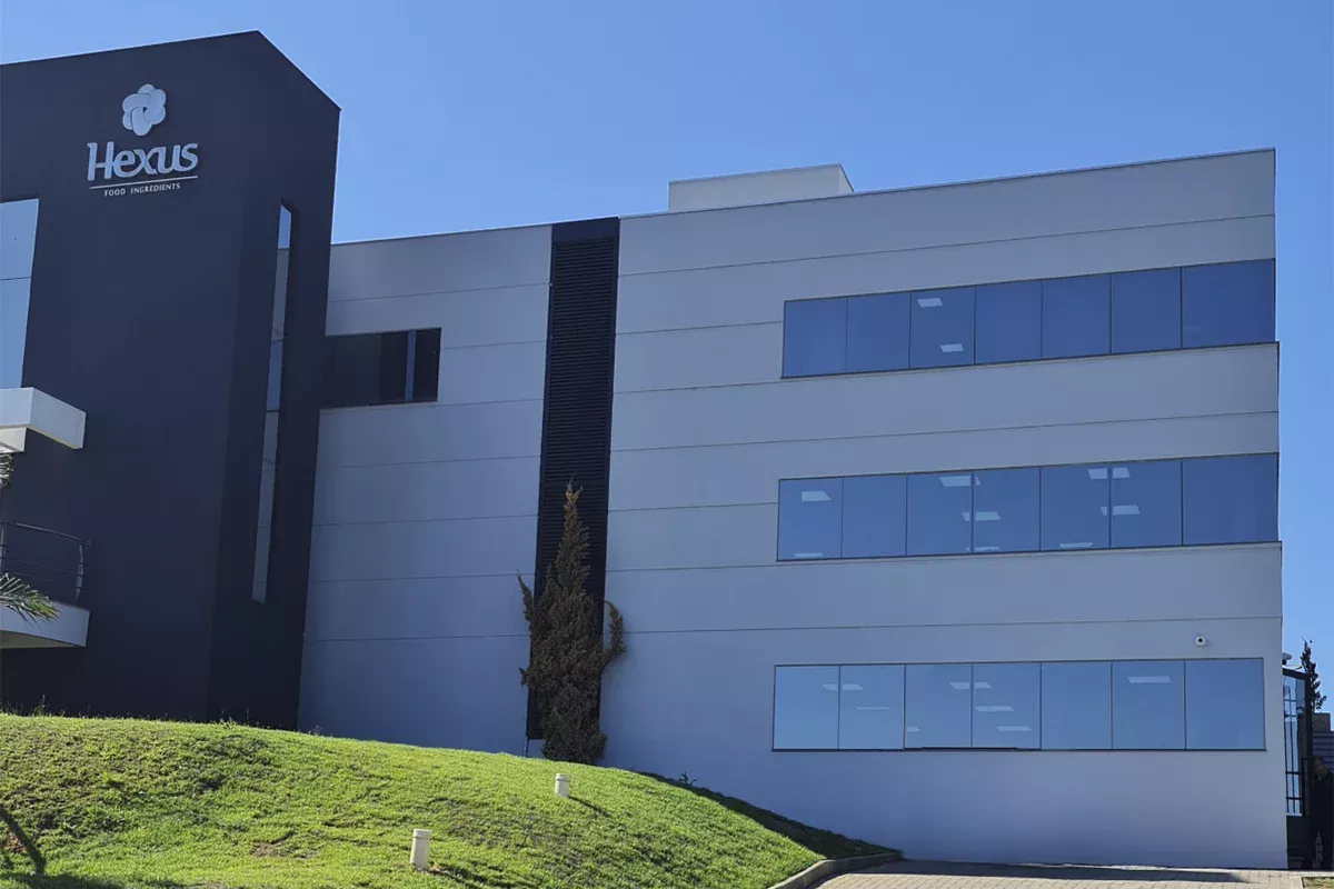 Obras casa Hexus - Fachada angular do edifício corporativo, destaque para arquitetura contemporânea e áreas verdes, evidenciando foco em performance e soluções inovadoras em projetos empresariais.