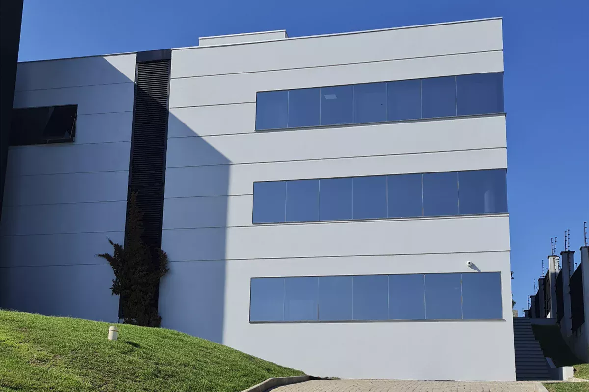 Obras casa Hexus - Fachada de edifício corporativo de três andares, grandes janelas de vidro e paisagismo frontal, simbolizando padrão elevado, inovação e Soluções em Comunicação assertivas.