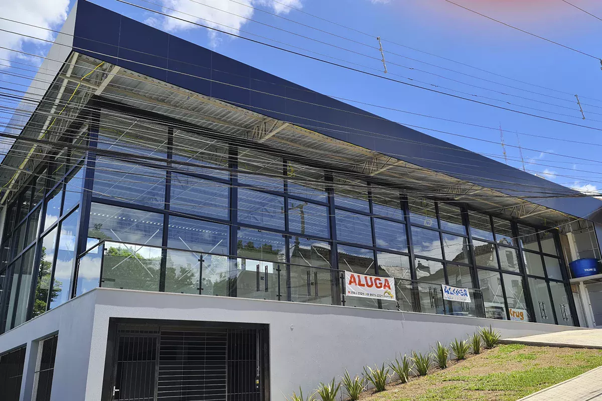 Obras casa Klauck - Detalhe da fachada envidraçada com letreiro de locação, jardim frontal e entrada acessível, evidenciando transparência, versatilidade e alinhamento aos objetivos do negócio.