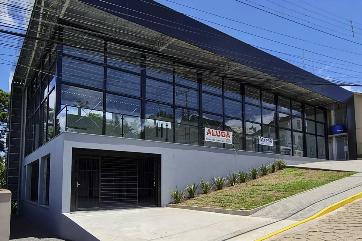 Obras casa Klauck - Fachada ampla com paredes de vidro e painéis metálicos, entradas bem definidas, paisagismo e estacionamento, reforçando inovação arquitetônica e foco em performance nos empreendimentos comerciais.