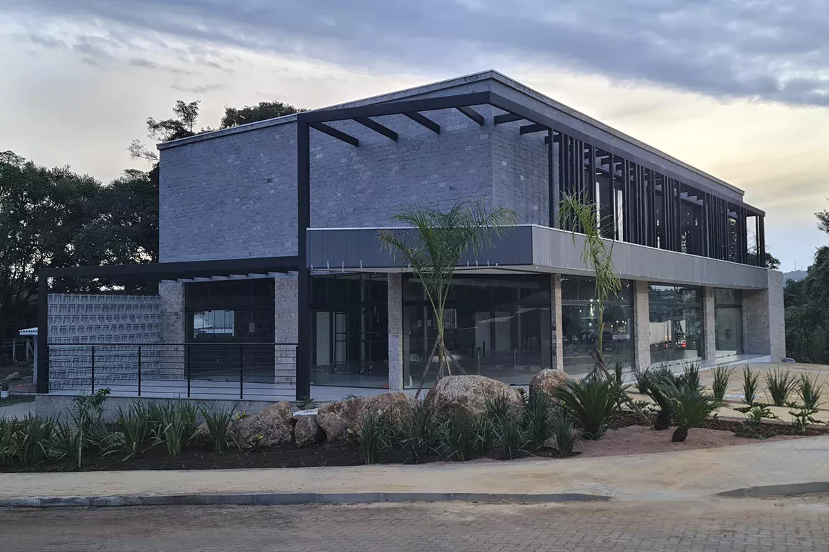 Obras casa Me - Vista angular de prédio comercial com painéis metálicos escuros, amplas áreas envidraçadas e paisagismo estratégico, demonstrando gestão comercial assertiva e alinhamento aos objetivos de negócio.
