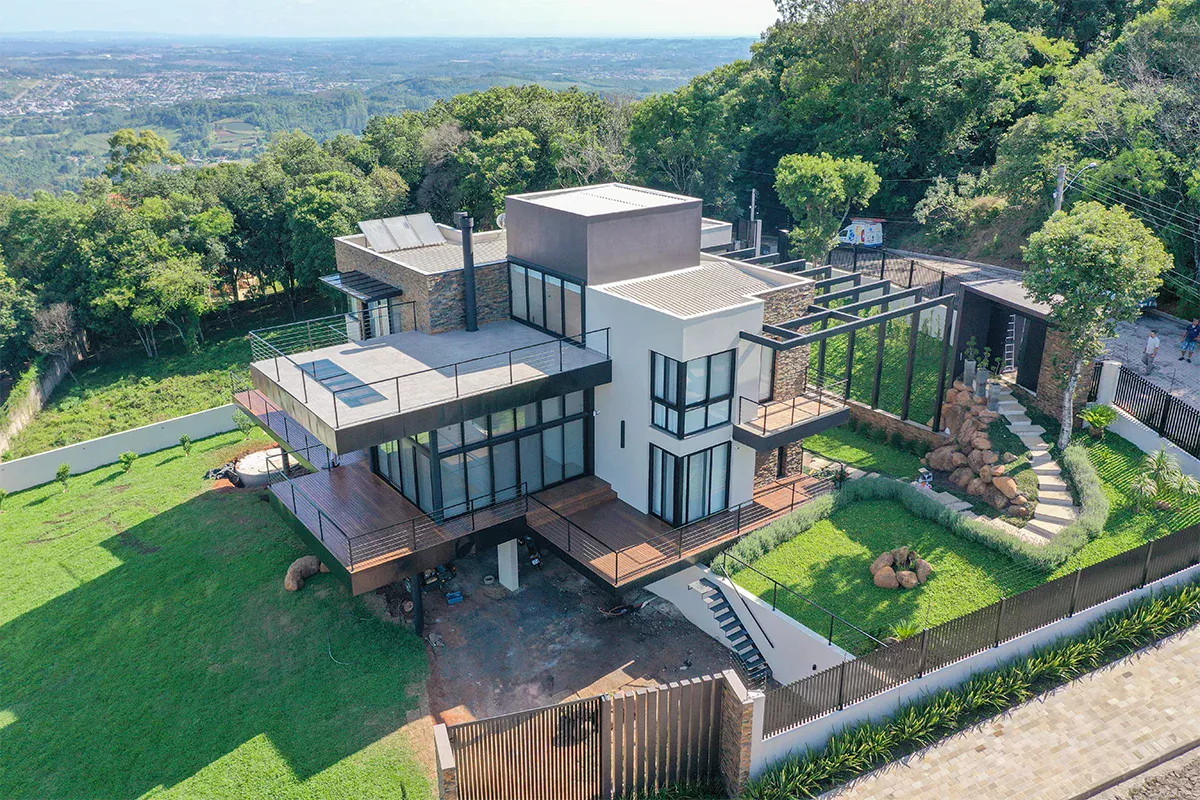 Obras casa MR - Vista lateral aérea de residência de alto padrão com decks em madeira e paisagismo, reforçando objetividade, personalização e expertise técnica.