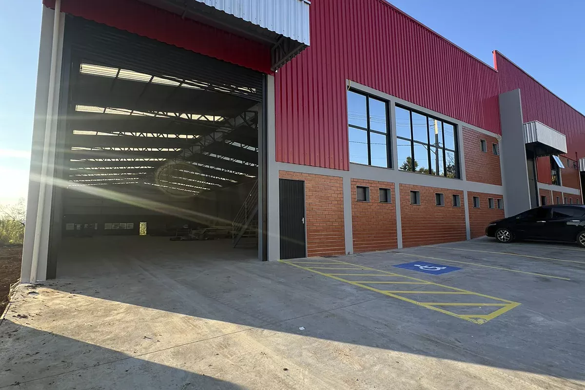 Obras casa Pavilhão Comercial - Entrada lateral do galpão, acessibilidade garantida por vaga demarcada e portas amplas sob estrutura metálica, reforçando objetividade e gestão comercial resolutiva.