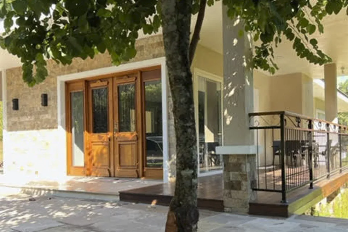 Obras casa J+S - Entrada principal de residência com porta de madeira, parede em pedra, varanda e vegetação, evidenciando acolhimento, inovação e atendimento resolutivo.