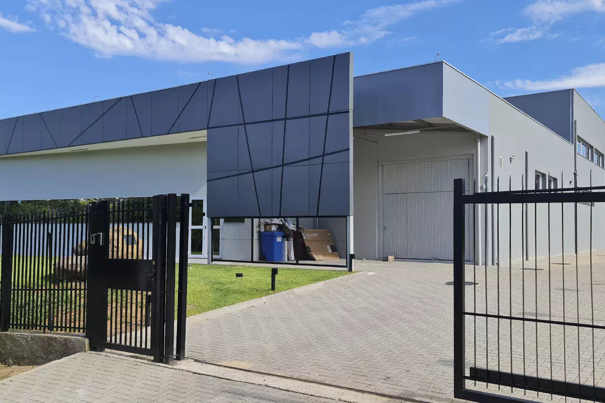 Obras Toth - Fachada de galpão industrial contemporâneo com painéis metálicos azuis, portão de acesso, piso de blocos intertravados e gramado lateral, evidenciando alto padrão construtivo e soluções em comunicação orientadas ao setor comercial.